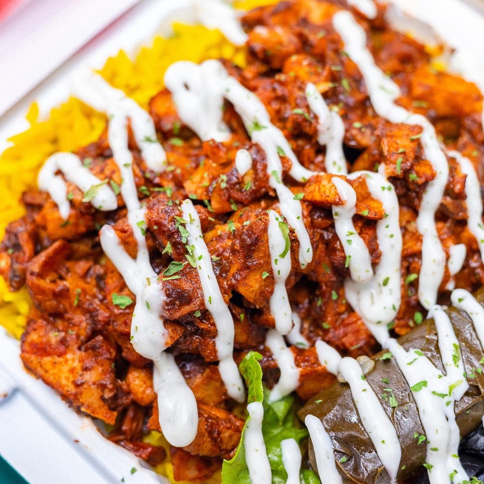 Vegan On The Fly's spicy vegan chicken, yellow rice, and stuffed grape leaves drizzled with white sauce.