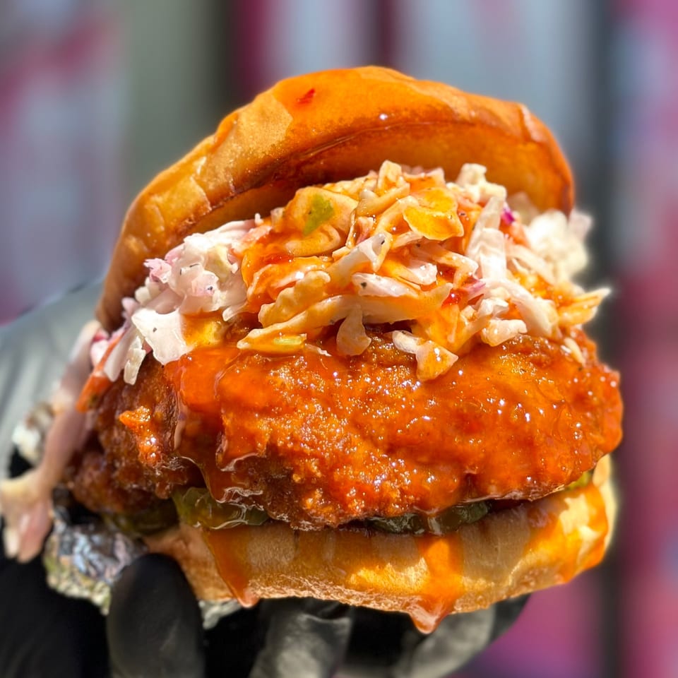 Close-up of a Vegan On The Fly vegan chicken sandwich with coleslaw and spicy sauce.