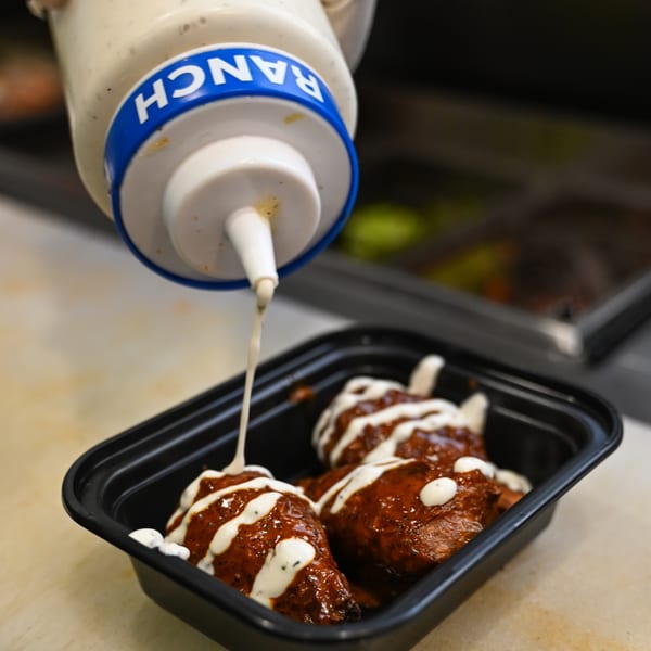 Vegan wings drizzled with ranch dressing from a squeeze bottle, in a black takeout container.