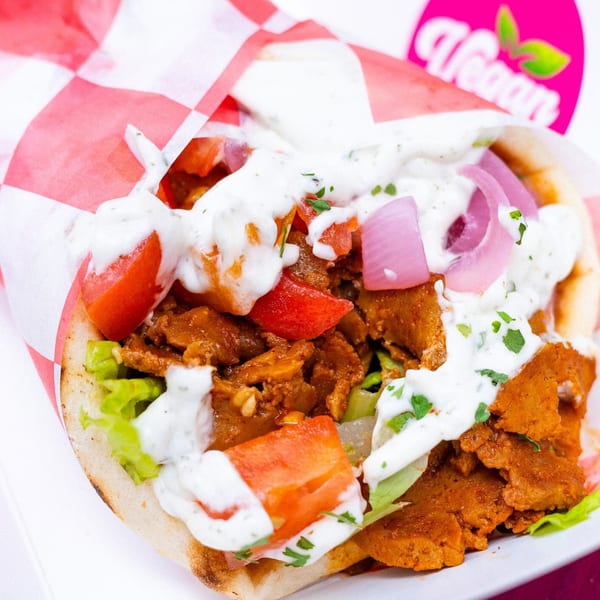 Vegan gyro with plant-based meat, lettuce, tomatoes, red onions, and white sauce in pita bread.