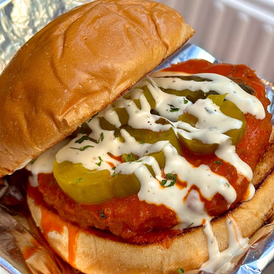 Vegan On The Fly's buffalo chicken sandwich with pickles, ranch, and hot sauce on a bun.