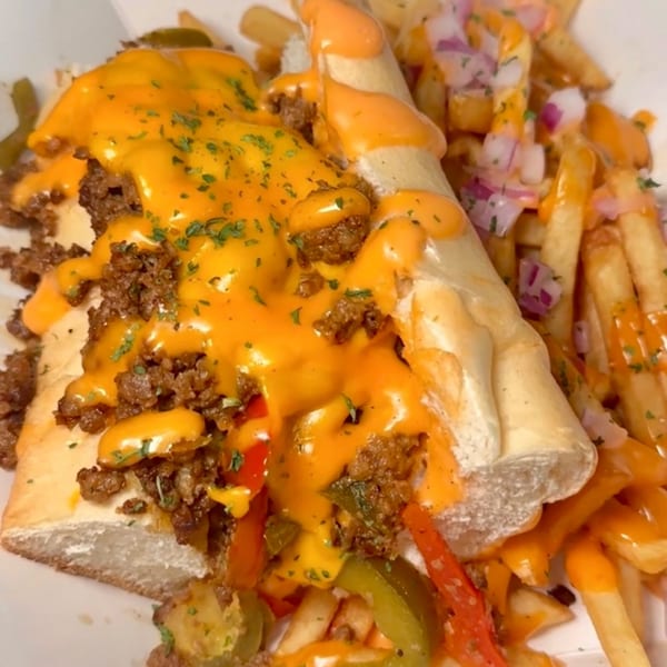 Vegan cheesesteak with melted cheese, peppers, and onions, served with fries.