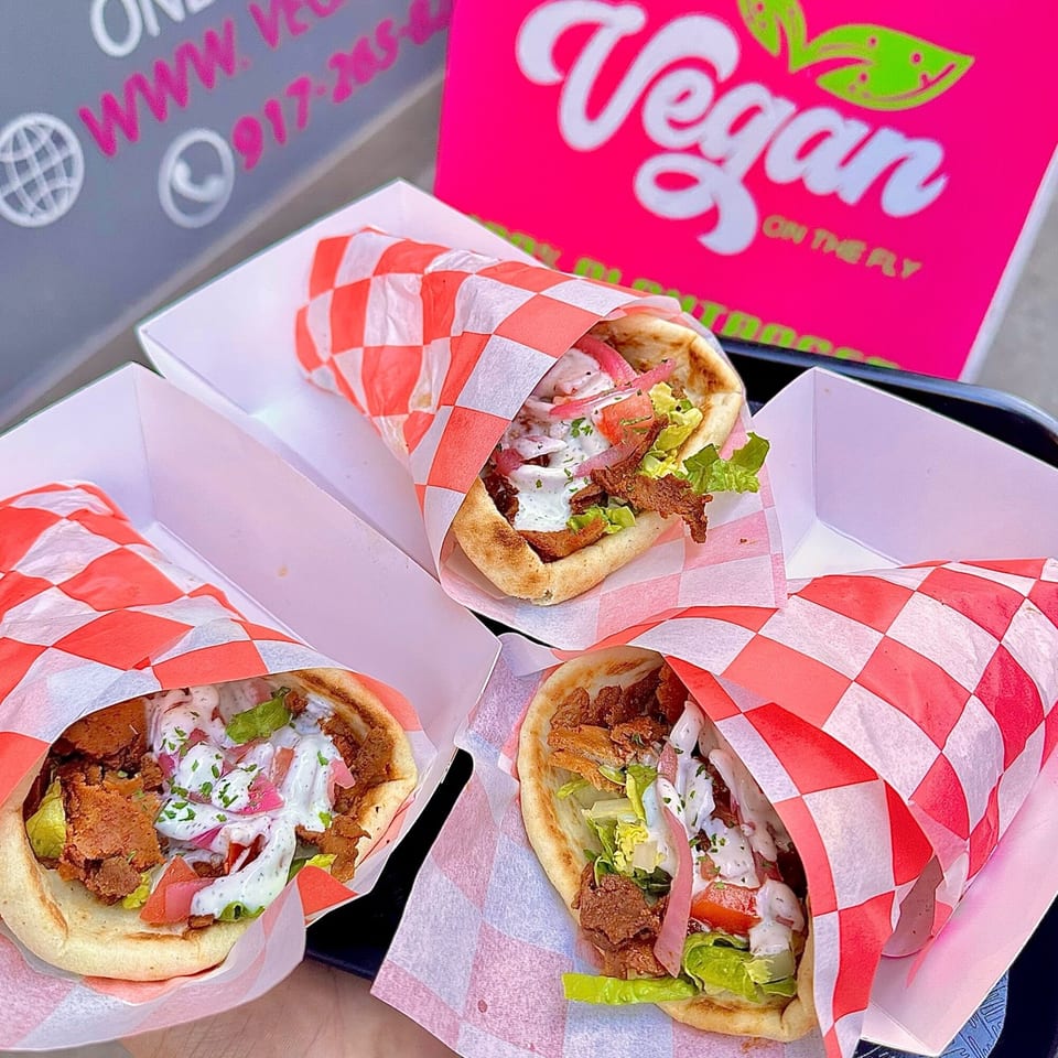 Three vegan gyros with plant-based meat, lettuce, tomatoes, pickled onions, and white sauce.