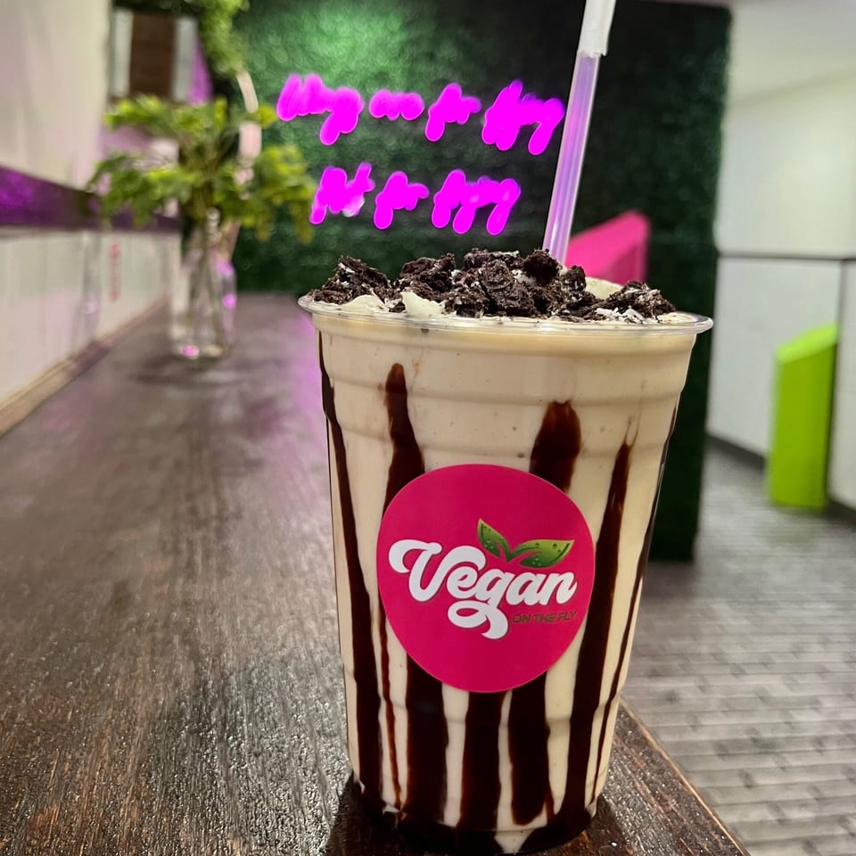 Vegan On The Fly milkshake with chocolate drizzle, cookie crumbles, and a pink neon sign.