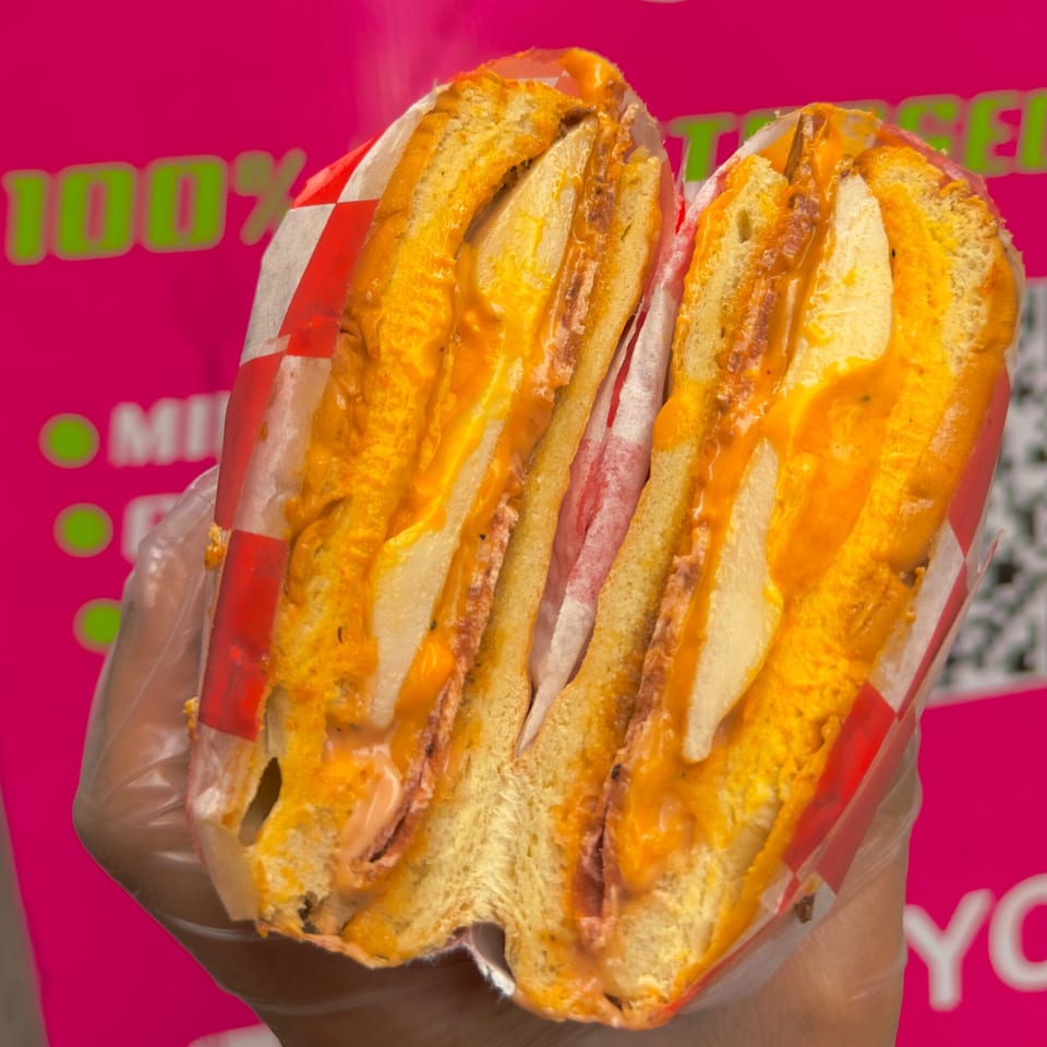 A vegan sandwich, cut in half, filled with fries and orange sauce, held against a pink background.
