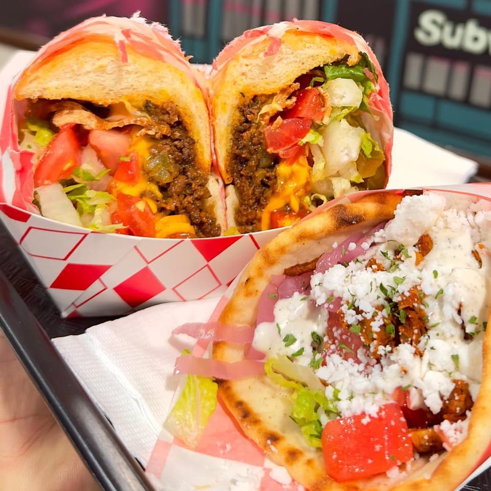 Two vegan subs, one cut in half, and a vegan gyro with feta, tomatoes, and lettuce.